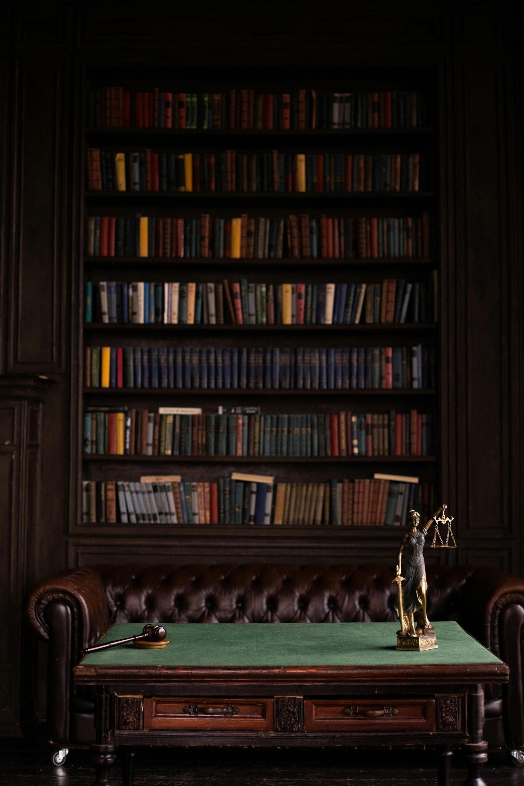 anasayfa A sophisticated library scene featuring a leather sofa, bookshelves, and a statue of justice with a gavel on the table.