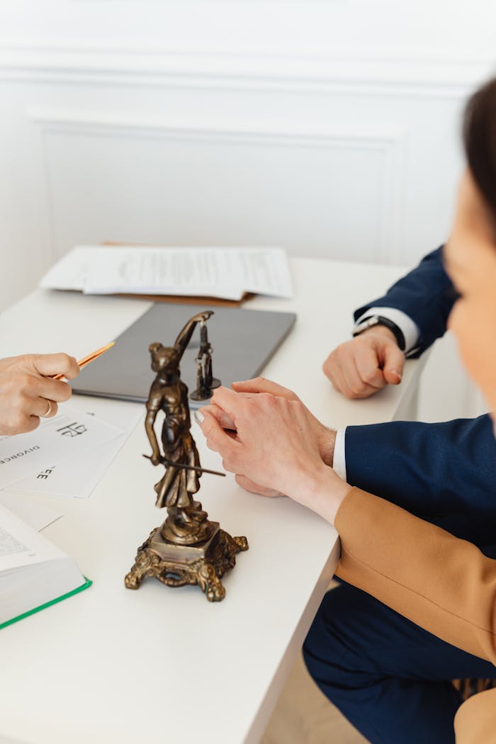 services-01 Legal professionals discussing documents with Lady Justice statue on desk.